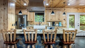A rustic kitchen with wooden cabinets, a stone backsplash, and a central island with bar stools.