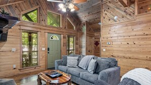 Un intérieur de chalet chaleureux avec un canapé gris, une table basse en bois et un ventilateur de plafond.