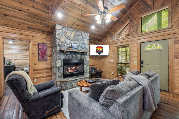 A cozy cabin interior with a stone fireplace, wooden walls, and a green door. - Hoot N Holler in Hochatown/Broken Bow, OK (Broken Bow)
