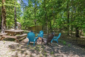 A picnic setup with a wooden table and chairs, surrounded by trees in a wooded area.
