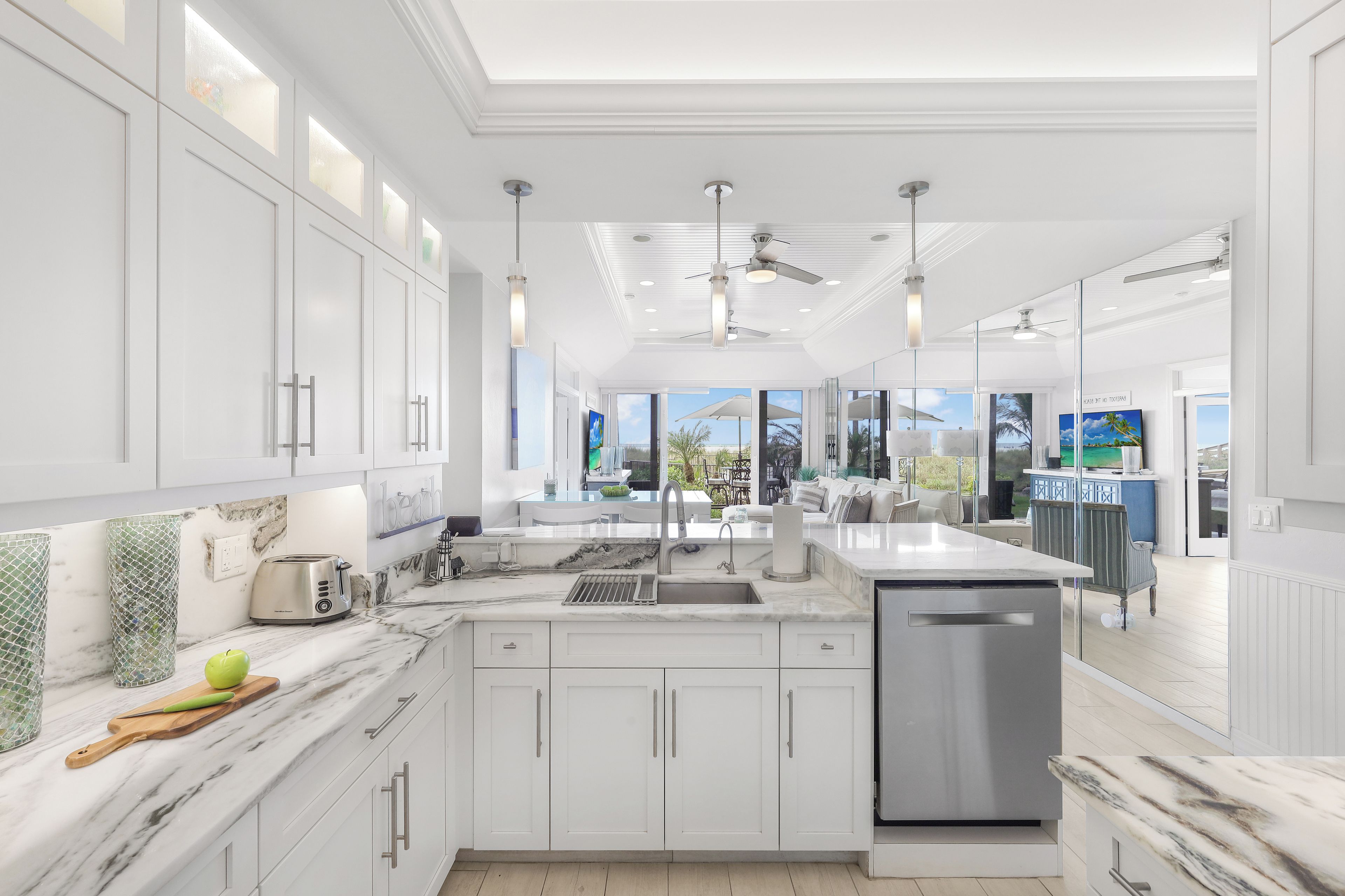 A modern kitchen with white cabinetry, a marble countertop, and a built-in dishwasher.
