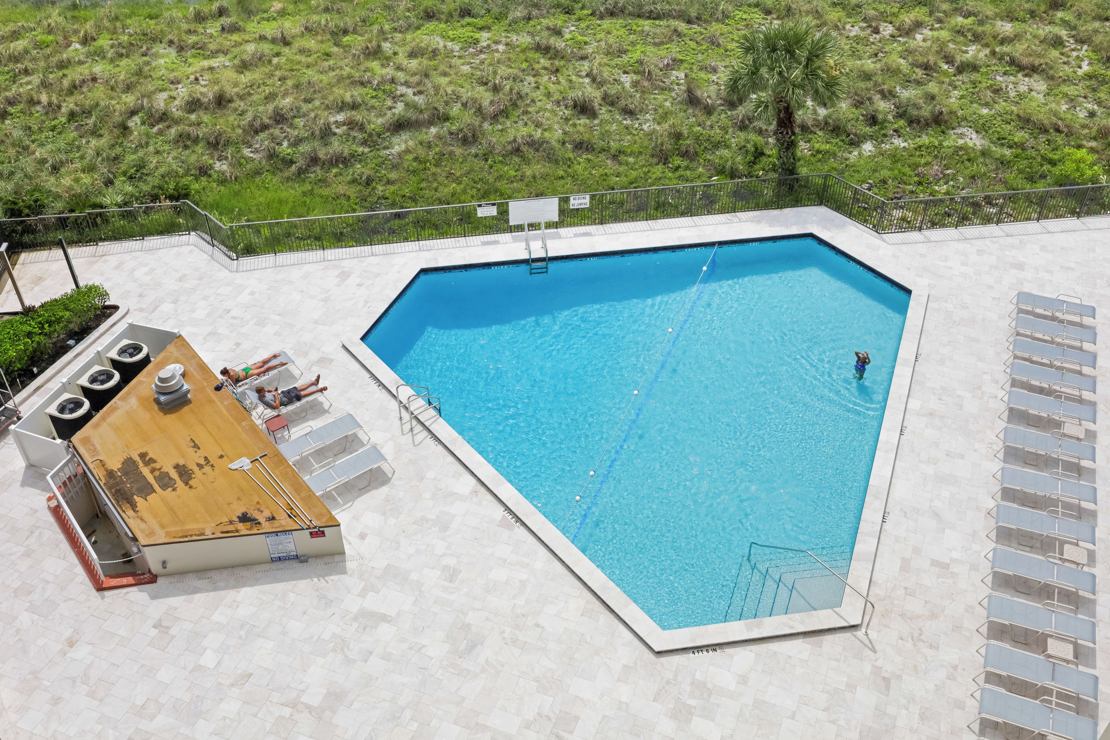 A swimming pool with a wooden deck area, lounge chairs, and a lifeguard stand.