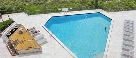 A swimming pool with a wooden deck area, lounge chairs, and a lifeguard stand.