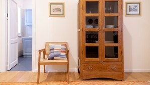 Um armário de madeira com portas de vidro, uma cadeira de vime com almofada listrada e um tapete estampado.
