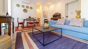 A living room with a sofa, coffee table, and dining area. - Planeta Palace - Junior Apartment (Palermo)