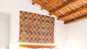 A neatly made bed with a colorful headboard, a patterned rug, and a wooden ceiling structure. - Planeta Palace - Apartment with terrace (Palermo)