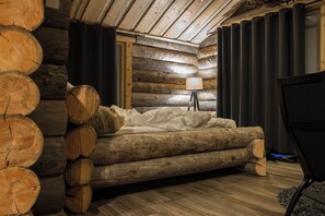 Het interieur van een blokhut met een bed, een lamp en een televisietoestel.