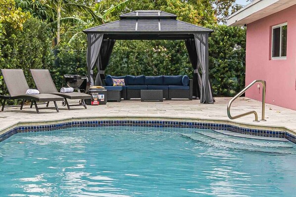 A pool area with a gazebo, lounge chairs, and a sofa.