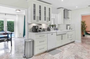 A modern kitchen with white cabinets, a marble countertop, and a coffee machine.