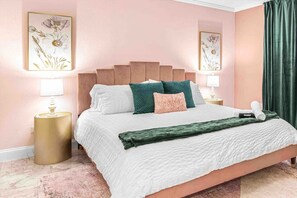 A bedroom with a pink wall, a wooden headboard, and a green throw blanket.