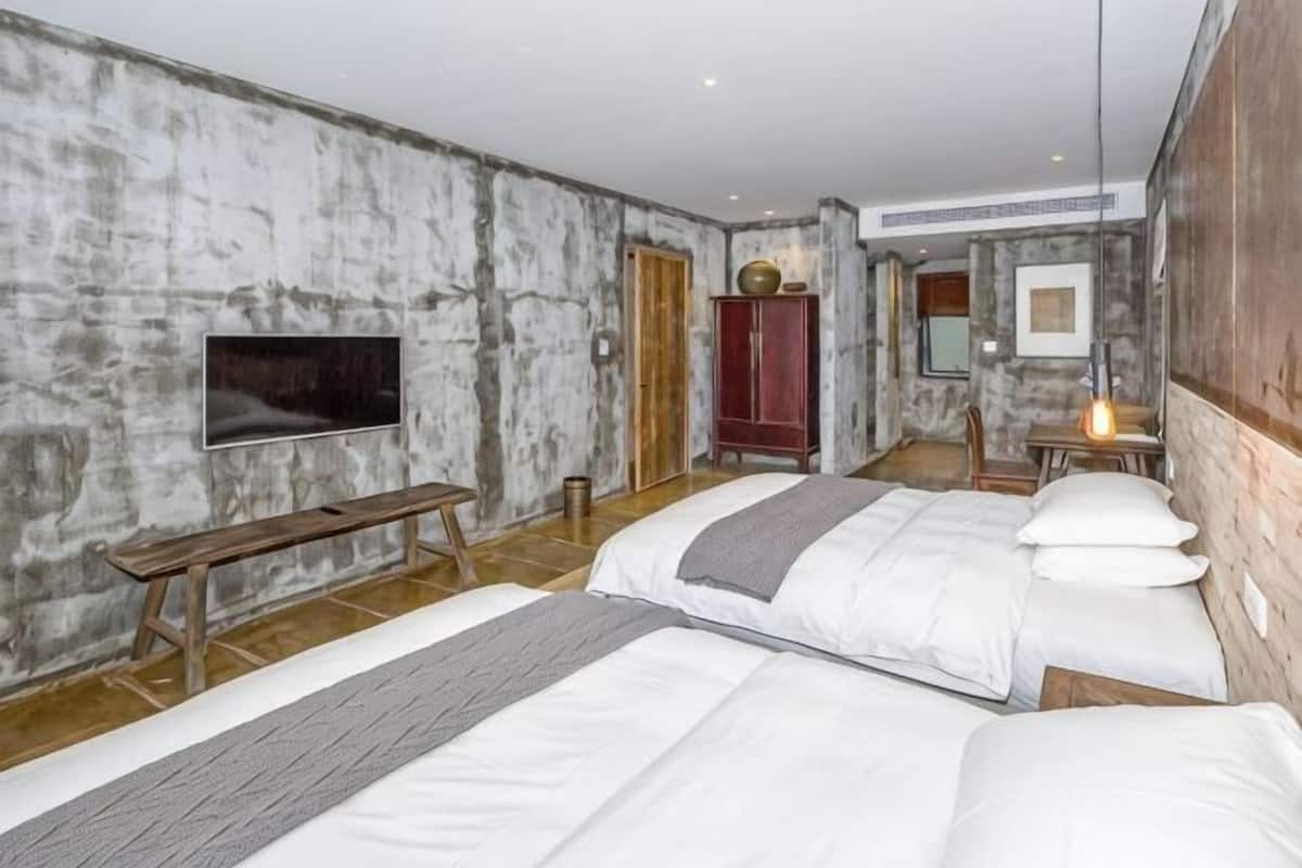 A bedroom with two beds, a bench, a TV, a wardrobe, and a table with a lamp.