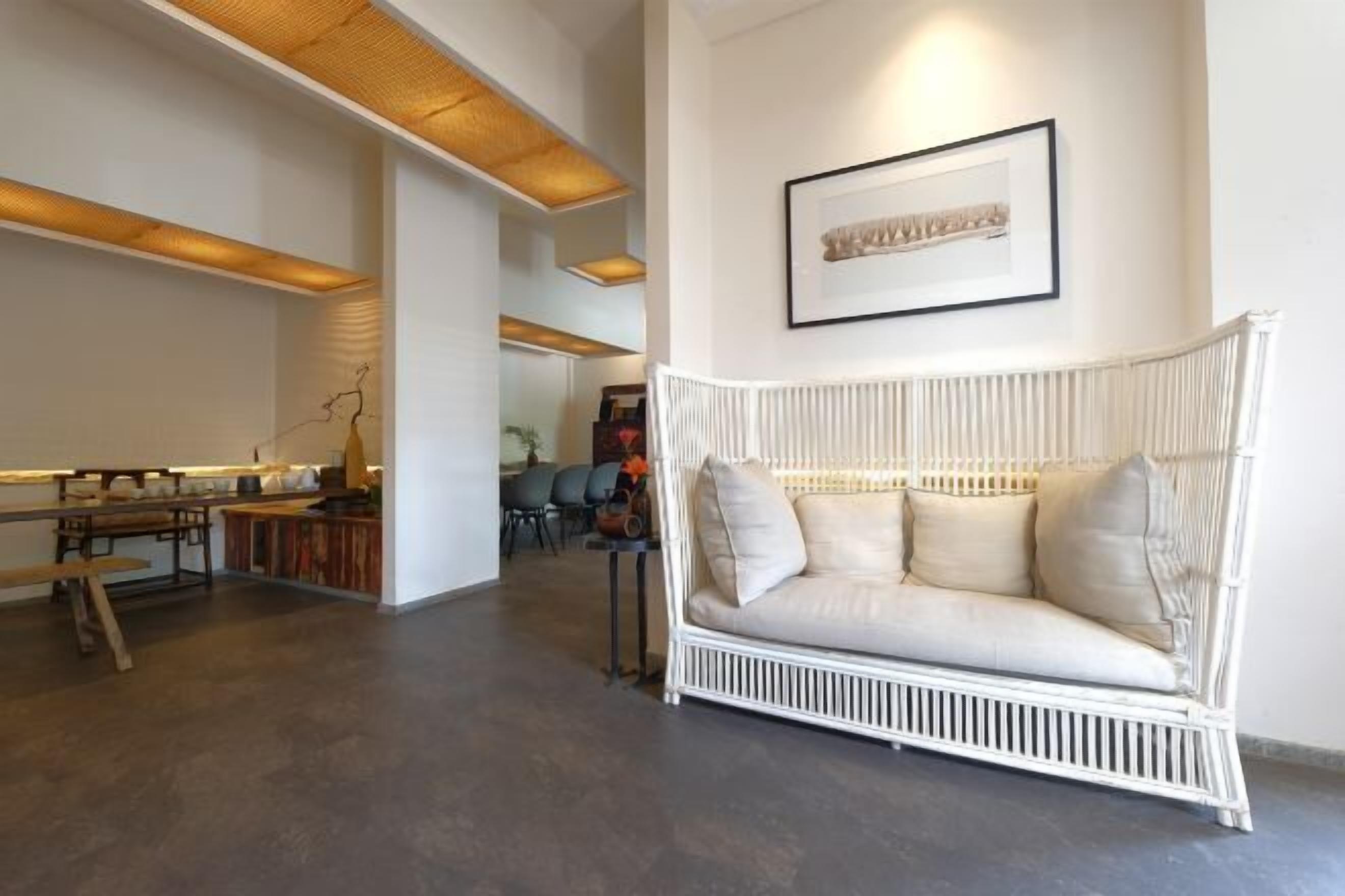 A modern living room with a white wicker sofa, a wooden bench, and a dining table.