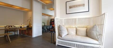 A modern living room with a white wicker sofa, a wooden bench, and a dining table.