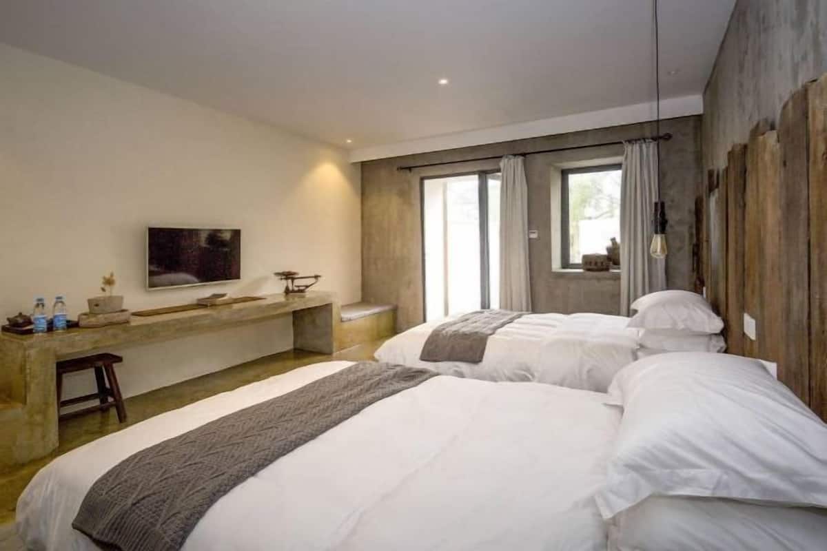 A modern bedroom with two beds, a TV, a desk, and a large window.