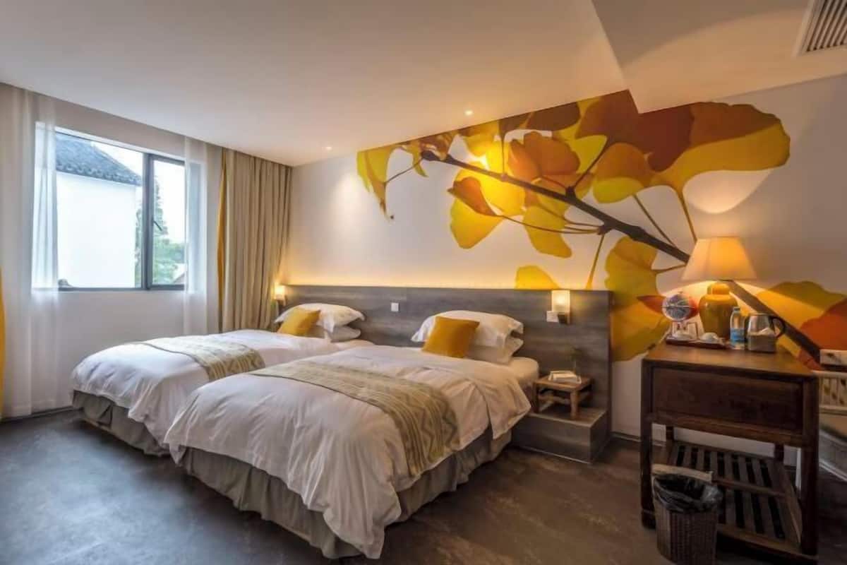 A hotel room with two beds, a large window, a wall mural, and a bedside table with a lamp.