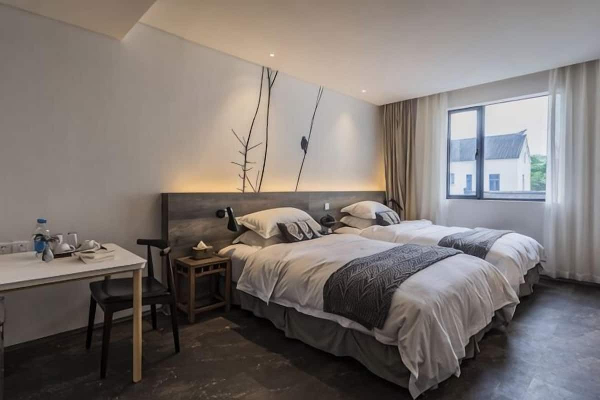 A hotel room with a bed, bedside table, lamp, and a window with curtains.