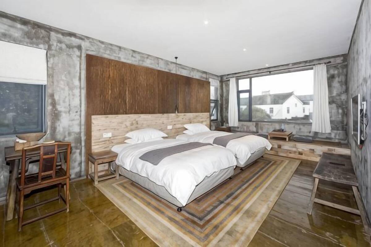 A bedroom with a large bed, a desk, and a view of buildings outside.