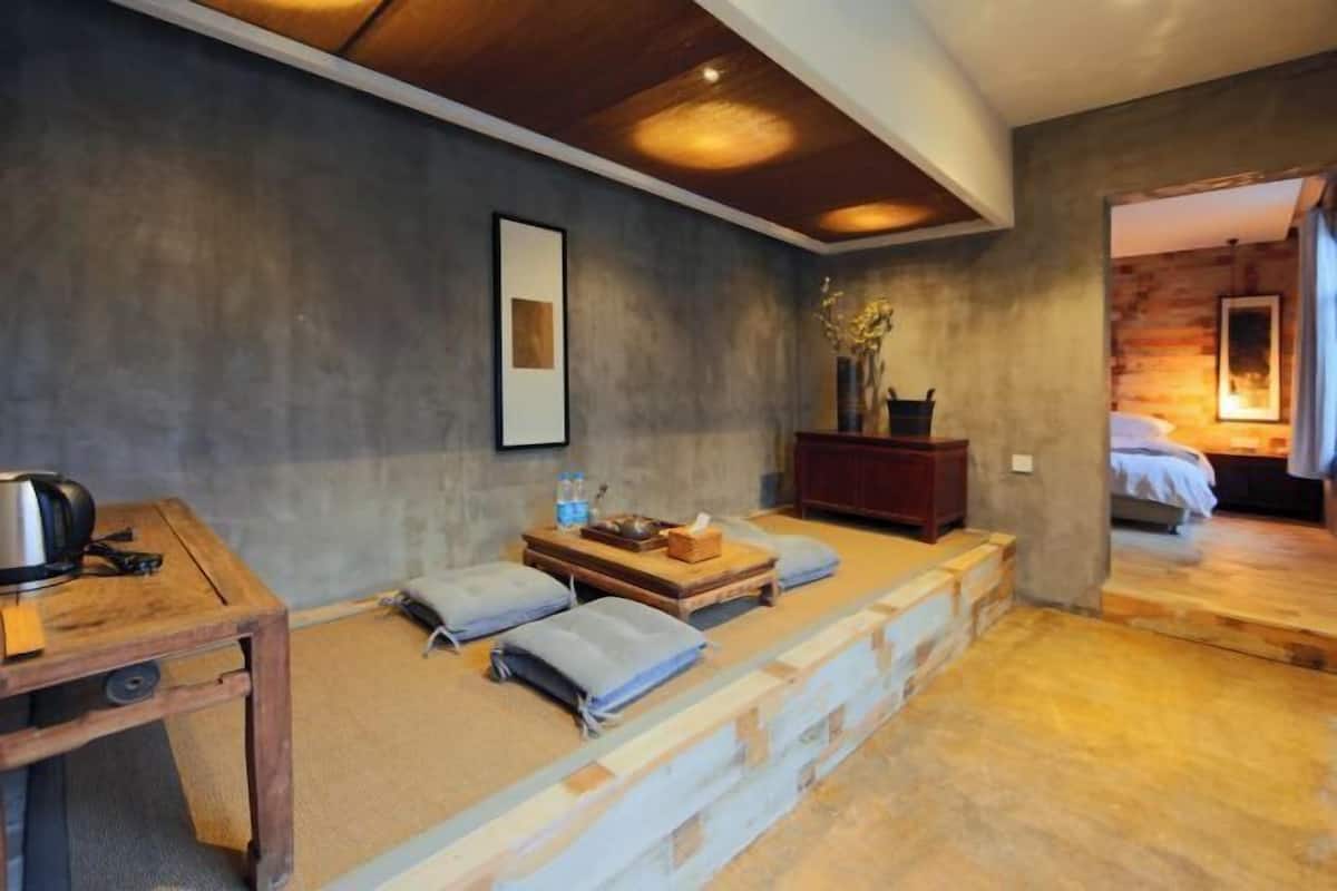 A cozy room with a wooden table, a sofa with cushions, a small wooden cabinet, and a staircase leading to another room.
