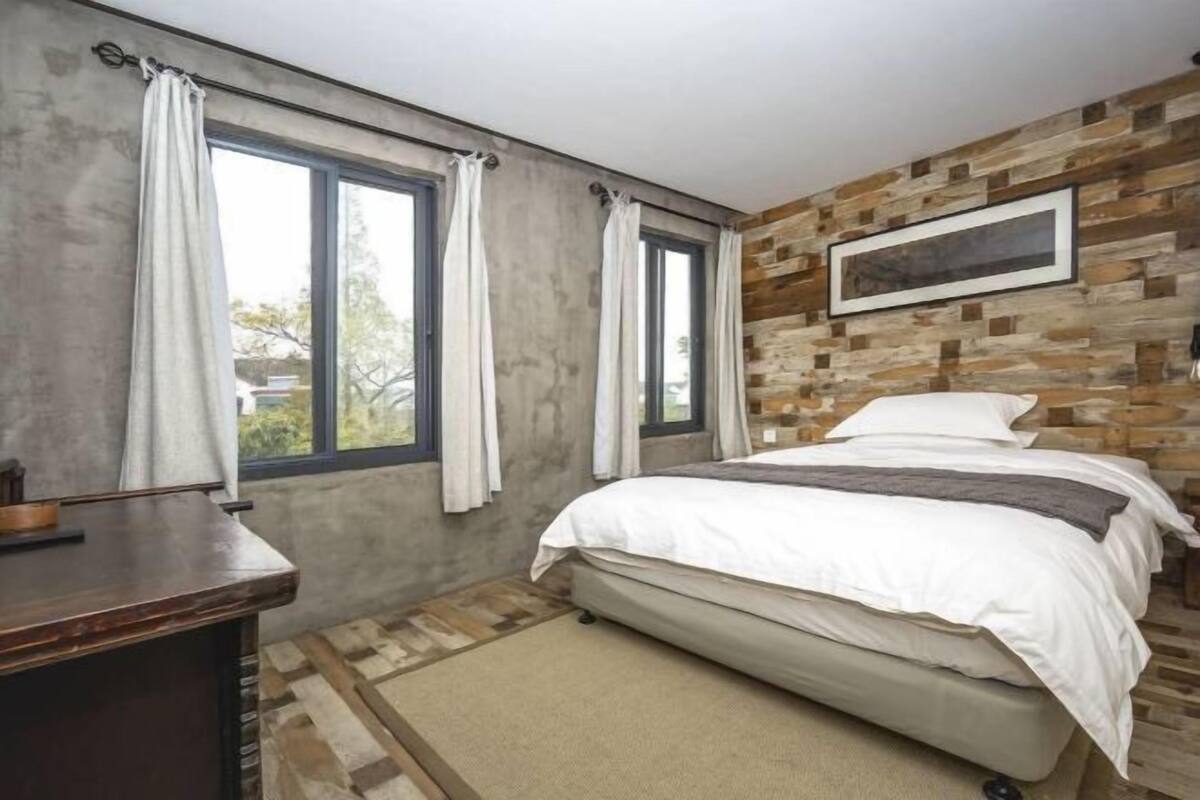 A bedroom with a bed, a desk, and a window with curtains.