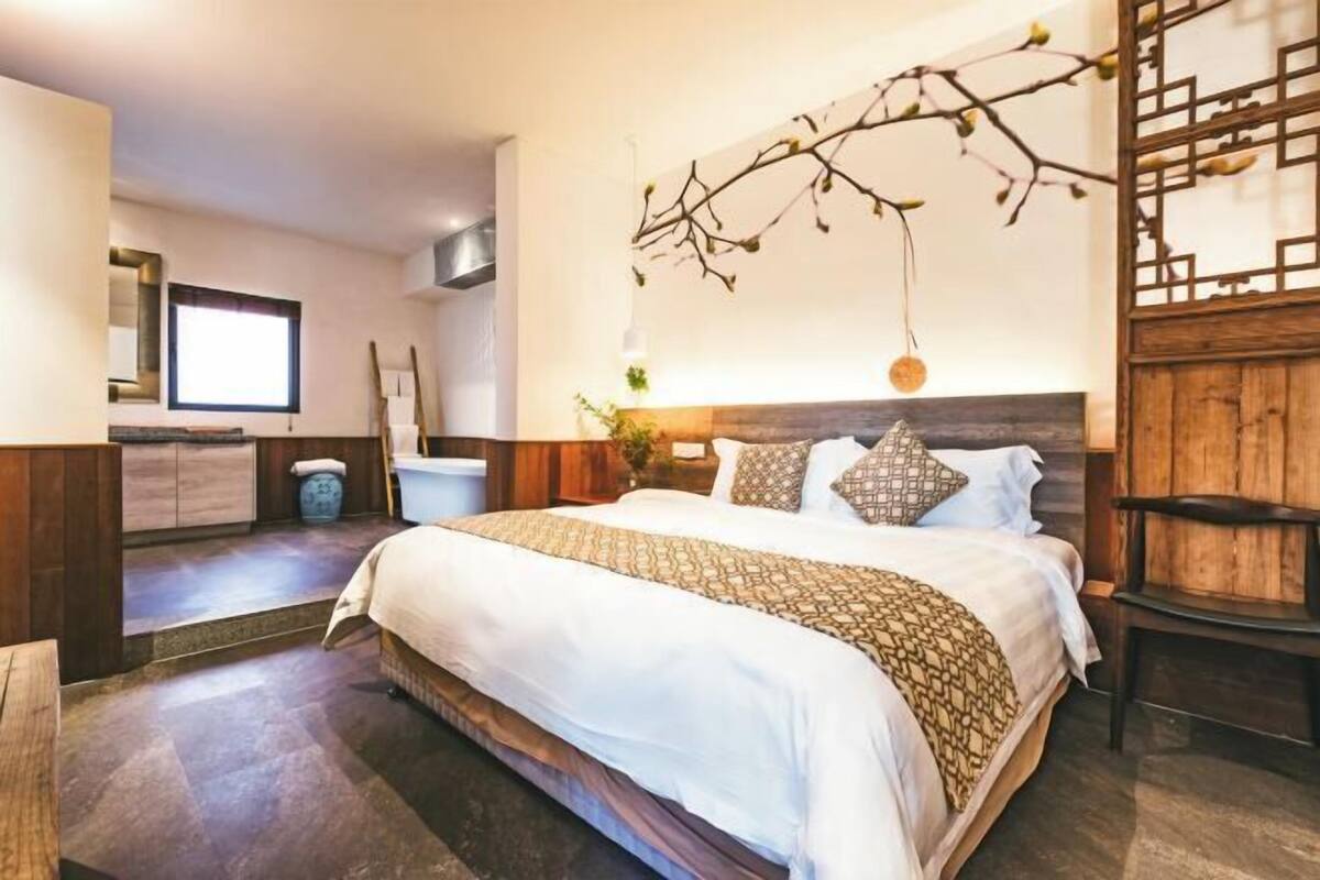 A bedroom with a large bed, a wooden headboard, a wall-mounted branch decoration, and a window.