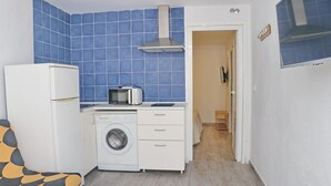 Une cuisine compacte équipée d’un lave-linge, d’un four à micro-ondes et d’un petit coin repas avec une chaise.