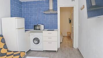 A compact kitchen with a washing machine, microwave, and a small dining area with a chair.