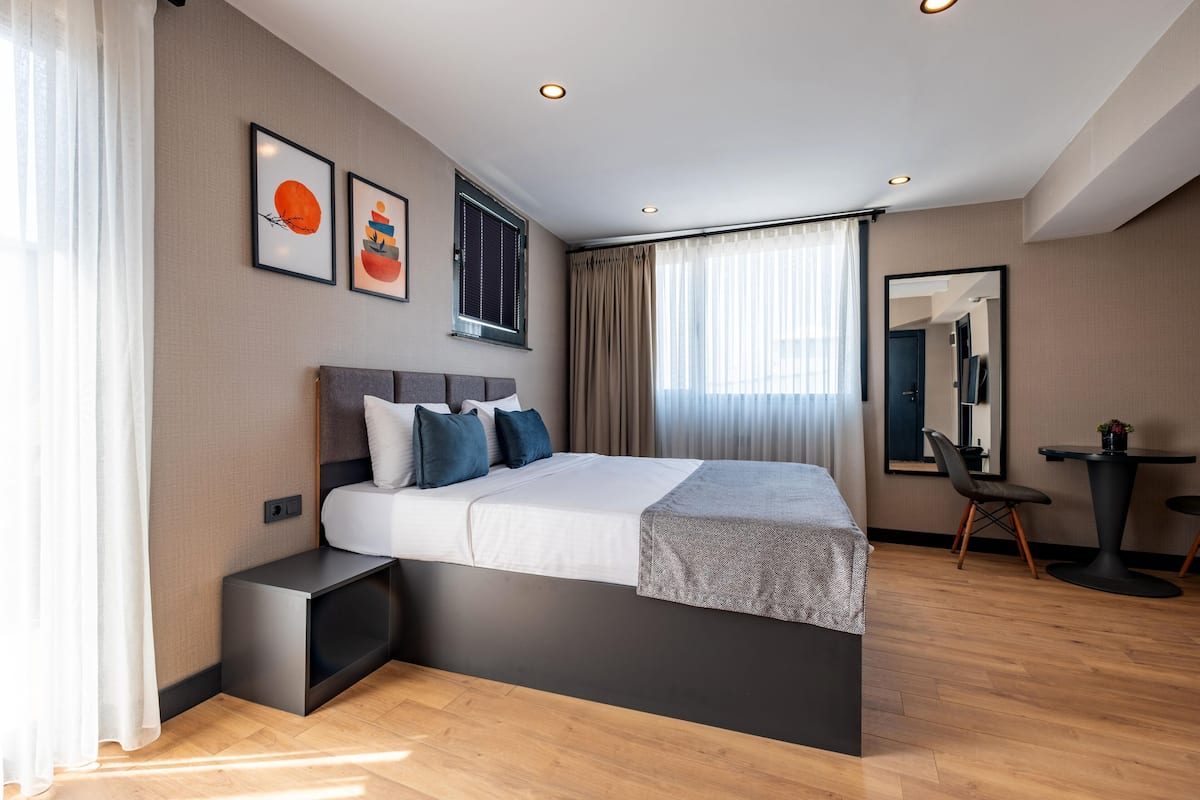 A modern hotel room with a large bed, bedside tables, a small desk, a chair, and a mirror.