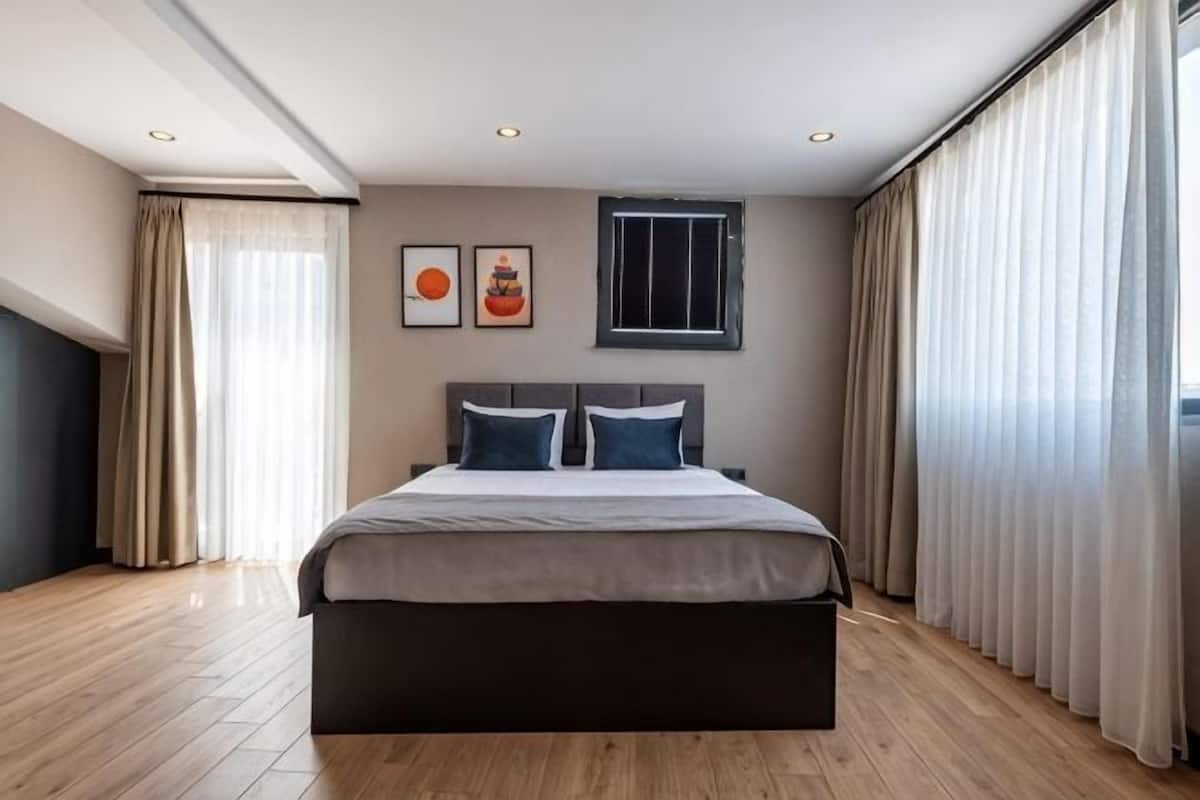 A modern bedroom with a large bed, a window, and curtains.