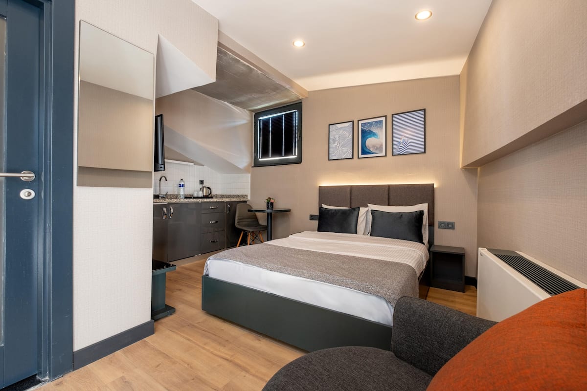 A modern hotel room with a bed, a desk, and a kitchenette.