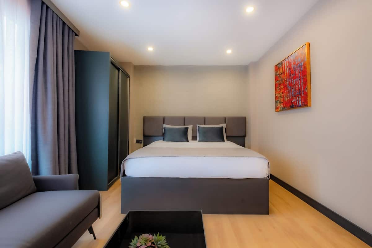 A modern hotel room with a large bed, a sofa, a small table with a plant, and a painting on the wall.