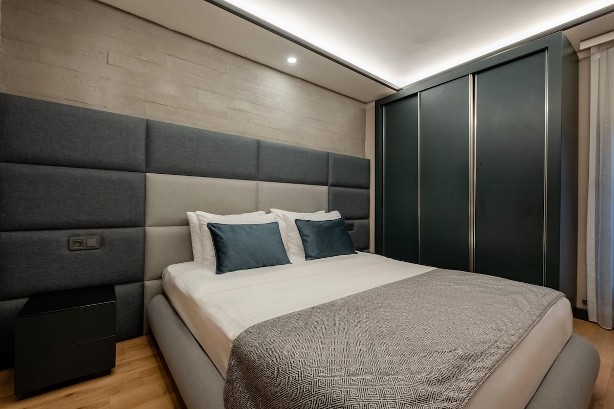 A modern bedroom with a large bed, built-in headboard, bedside tables, and a wardrobe.