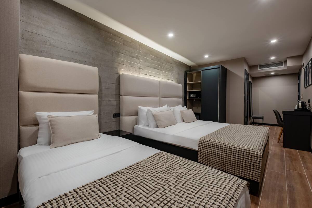 A hotel room with two beds, a wooden accent wall, a desk, and a chair.