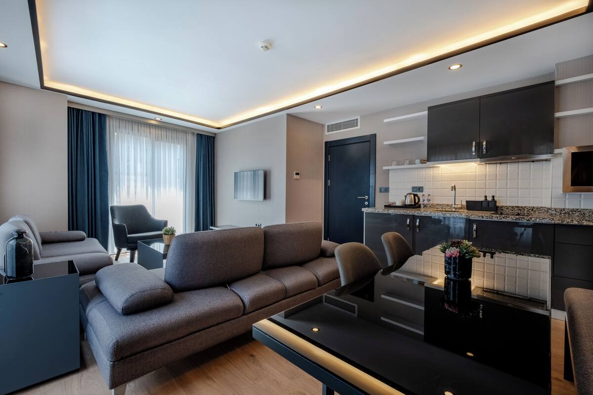 A modern living room with a sofa, a coffee table, and a kitchen area with a countertop and cabinets.