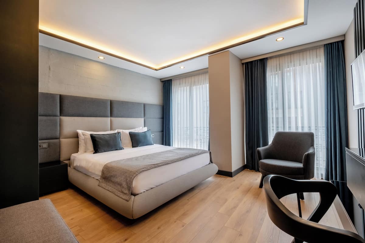 A modern hotel room with a large bed, a seating area, and a view of the city.