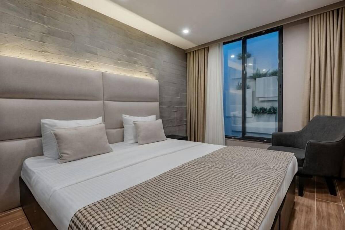 A modern hotel room with a large bed, a sofa, and a view of the outdoors.