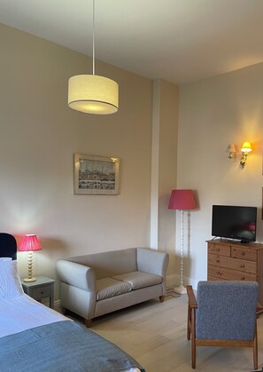 A hotel room with a bed, a sofa, a TV on a wooden cabinet, a lamp, and a wall-mounted picture.