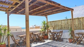 Una pérgola de madera con mesas y sillas en una terraza en la azotea con vistas a la ciudad.