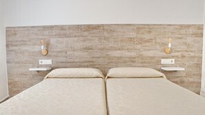 Una cama doble con cabecera de madera, dos mesitas de noche y lámparas de pared.