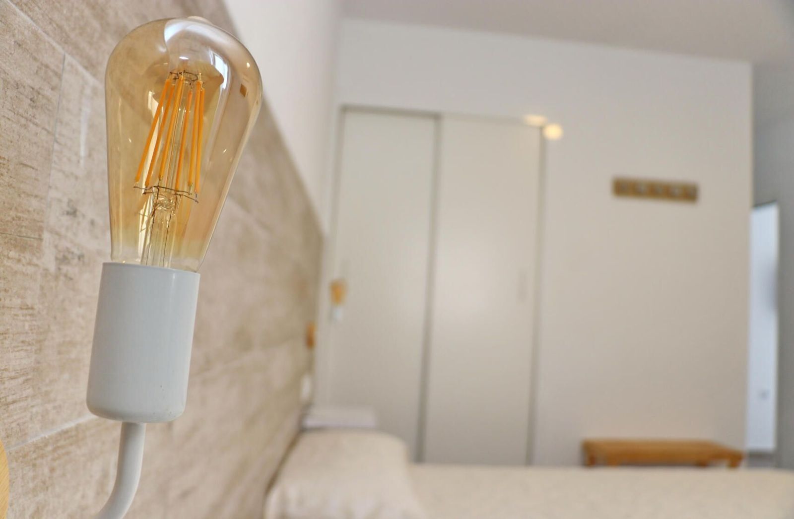 Una habitació d'hotel amb llit, una tauleta de nit i una làmpada penjada a la paret.