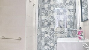 Un baño con baldosas estampadas, cabina de ducha de cristal, lavamanos blanco y pasamanos.
