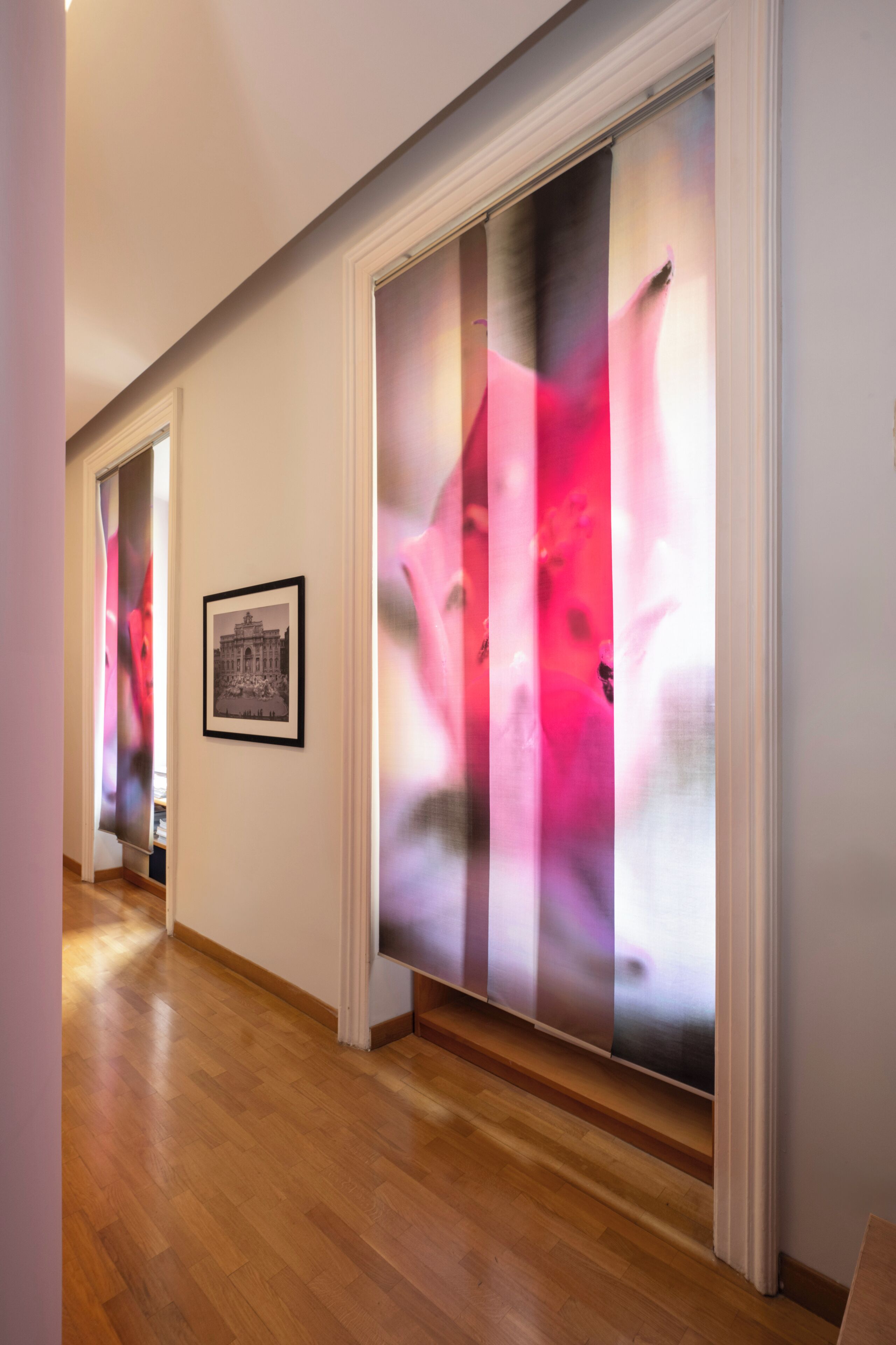 A hallway with wooden flooring, a framed picture on the wall, and a large abstract painting.