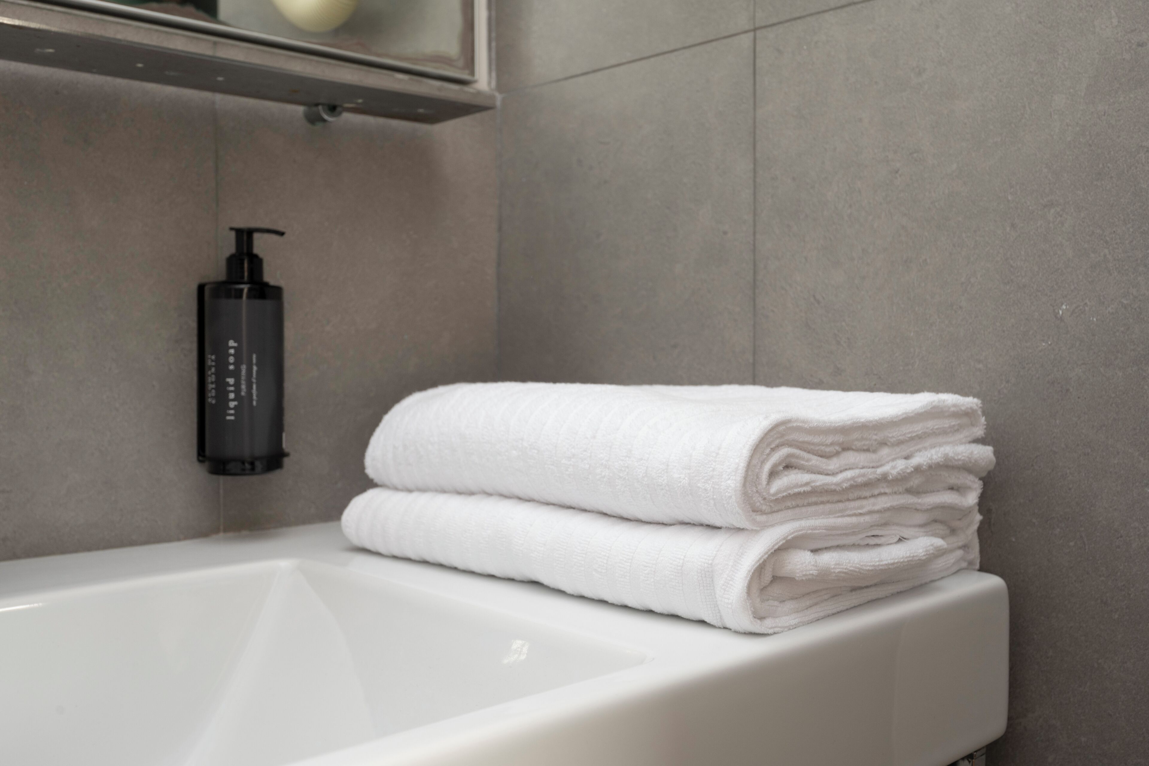 A bathroom with a white bathtub, a black soap dispenser, and a stack of white towels.