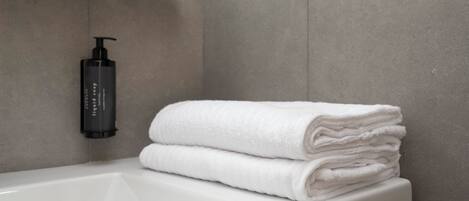 A bathroom with a white bathtub, a black soap dispenser, and a stack of white towels.
