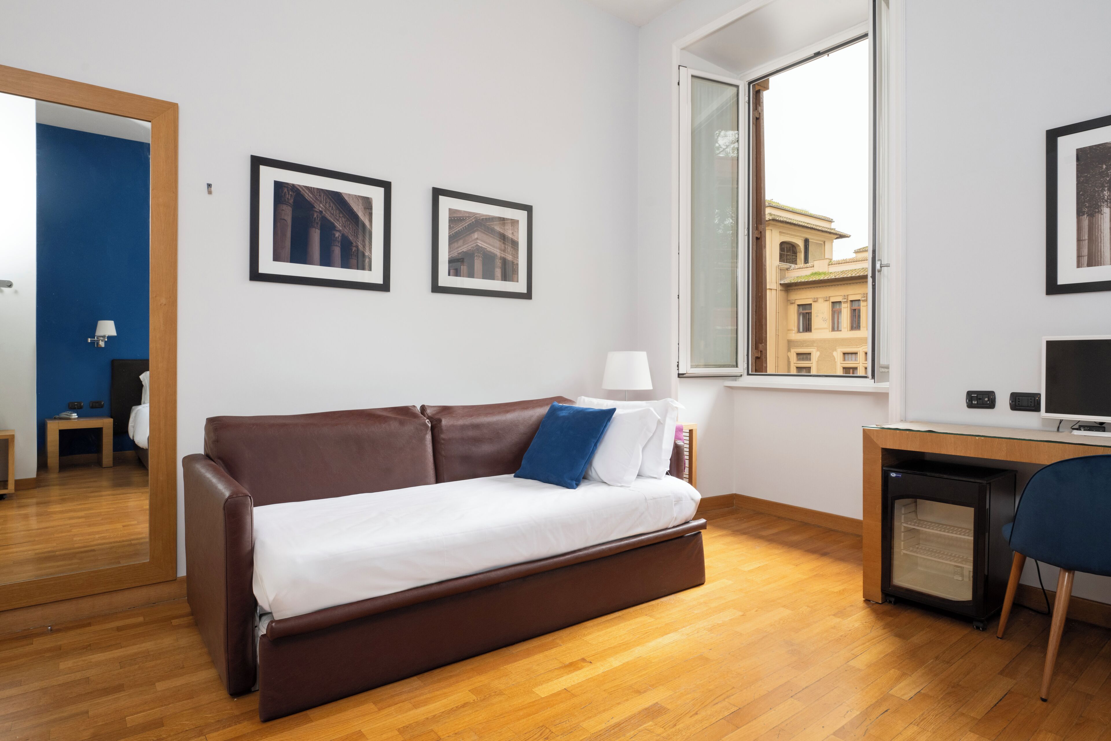 A modern room with a brown sofa, a small desk, a chair, and a window with a view of buildings.