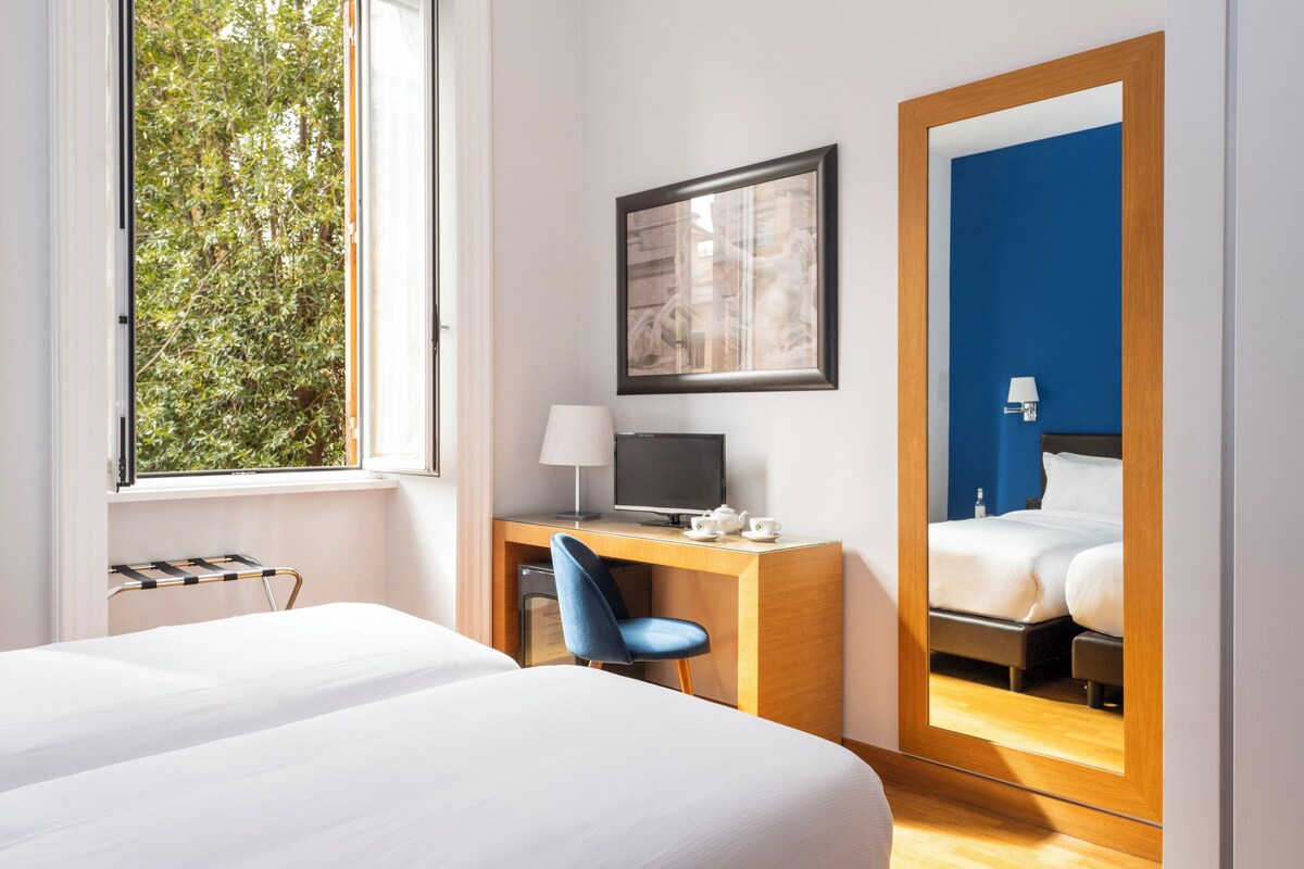 A hotel room with a bed, a desk with a chair, a TV, and a mirror.