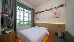 A hotel room with a bed, a sofa, a wooden nightstand, a window with curtains, and wall-mounted artwork. - Yunshuiyao Yunshui Guest House (Nanjing County)