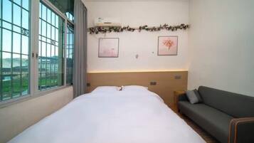 A hotel room with a bed, a sofa, a window with a view, and two framed pictures on the wall.