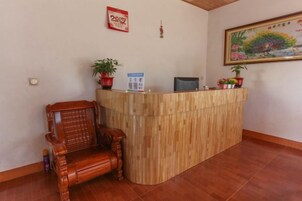 A reception desk with a wooden finish, a wooden chair, and a potted plant.