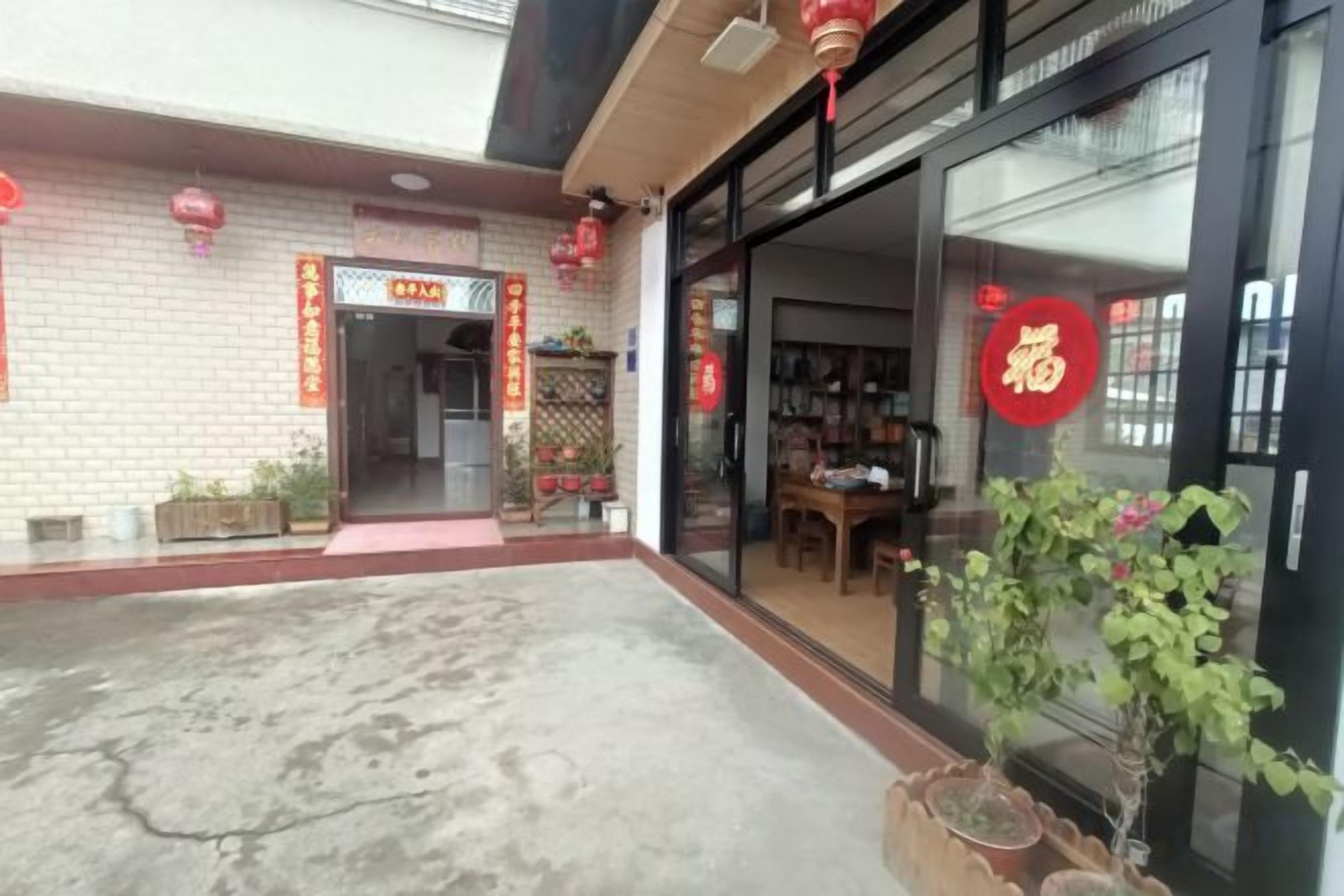 A storefront with a red sign, a glass door, and potted plants outside.