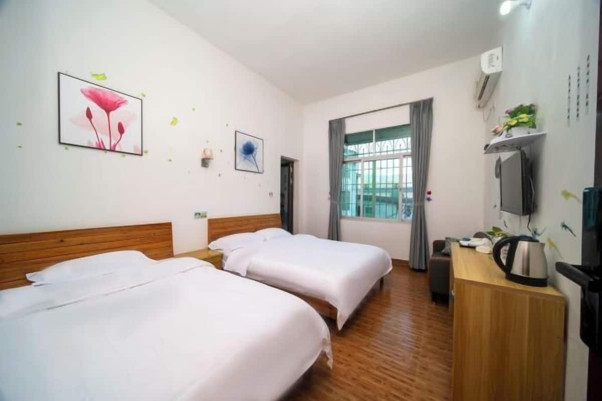 A hotel room with two beds, a wooden headboard, a desk with a kettle, a TV, and a window with curtains.